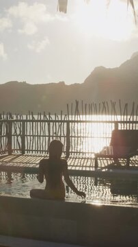 Luxury travel vacation resort hotel pool. woman tourist relaxing watching sunset on private balcony terrace of overwater bungalow suite in Bora Bora, Tahiti, French Polynesia. Raw real vertical video