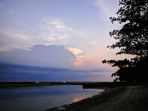 Serene tropical beach at sunset with soft purple and orange pastel skies and calm water reflection