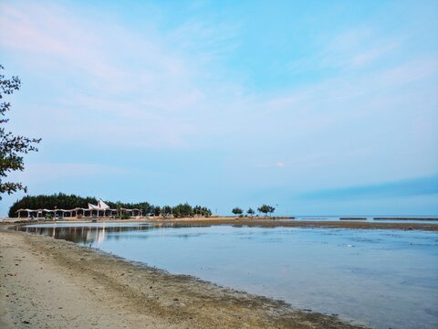 Calm coastal beach landscape at low tide featuring blue sky and gentle reflections on wet sand surfaces