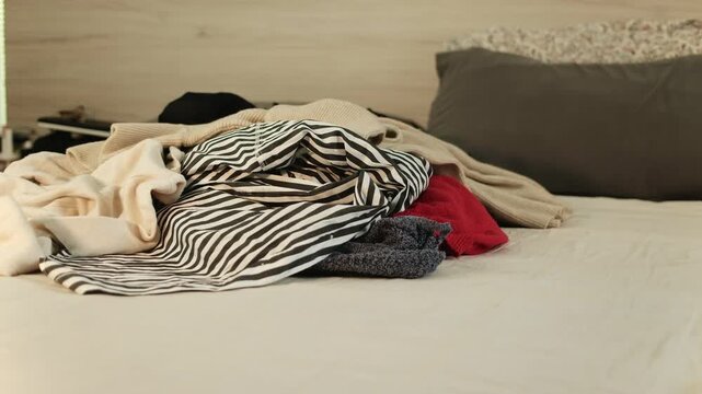 Tossing a loose pile of warm clothes onto a bed during an autumn and winter wardrobe cleanout, capturing an authentic seasonal decluttering and home organization routine.
