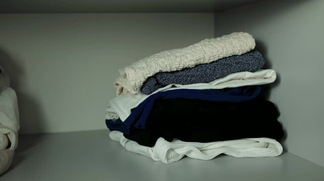 Placing a neatly folded stack of warm clothes into a wardrobe shelf while organizing an autumn and winter wardrobe, illustrating seasonal storage, decluttering and efficient home organization.