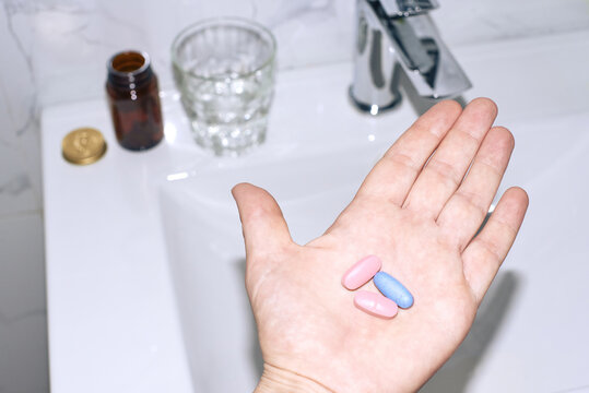 Hand holding pills near sink and glass of water