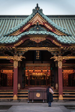 Bunkyo City, Tokyo, Japan - 04 December 2019: View of Nezu Shrine with its ornate red and gold architecture, intricate roof details, and a person standing in prayer.