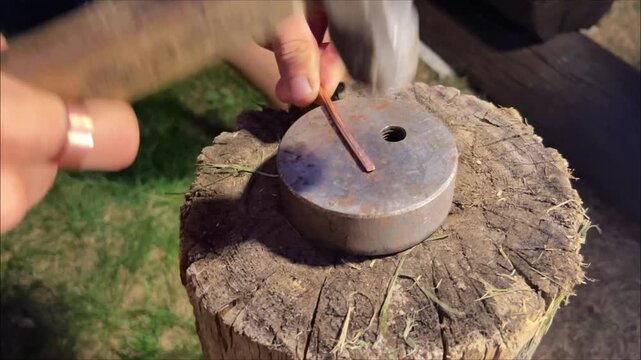 Action close up shot of a hammer striking a narrow copper metal strip on a round steel anvil outdoors. Metalworking DIY handcrafting concept.