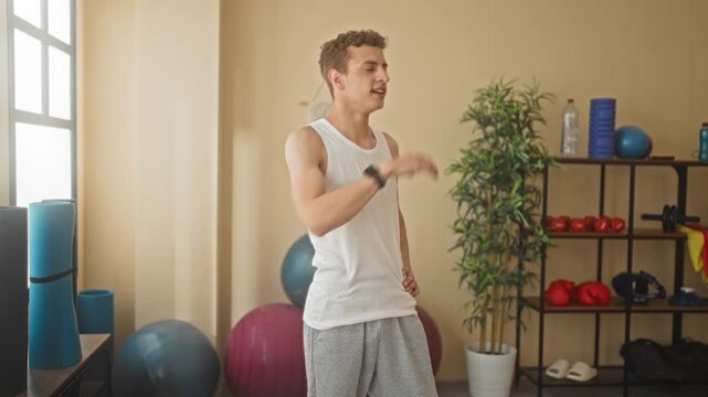 Young man in tank top wipes forehead with hand in a fitness studio after exercise; post workout fatigue.