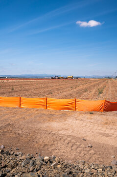 Eugene, Oregon, United States - 16 August 2026: View of the Amazon warehouse construction site near Eugene Airport, with orange safety fencing, cleared earth, and distant hills.
