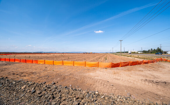 Eugene, Oregon, United States - 16 August 2026: View of the construction site for the new Amazon warehouse center near Eugene Airport, featuring a large cleared field with orange fencing.