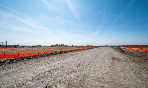 Eugene, Oregon, United States - 16 August 2026: View of the Amazon warehouse construction site near Eugene Airport, featuring cleared land, orange safety fencing, and a gravel road.