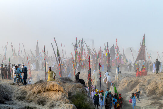 Okara, Punjab, Pakistan - 13 March 2024: View of the annual Urs and mela at the shrine of Sufi saint Hazrat Daud Bandagi Kirmani, with devotees gathering amidst colorful flags and dusty terrain.