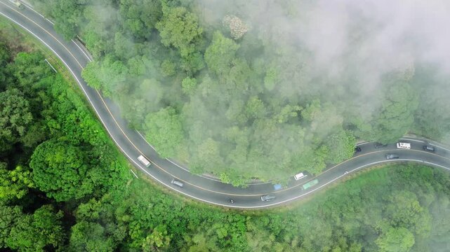 Aerial view of the winding road through lush forest near Panatapan Berastagi with misty conditions and vehicles, Berastagi, North Sumatra, Indonesia.