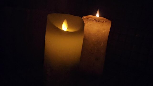 Candlelight fills the space as two candles flicker softly in a dark room at night
