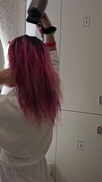 Woman dries her hair with a hair dryer in a bright bathroom after a shower in the morning