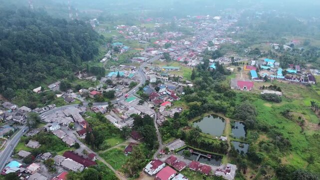 Aerial view of the town of Berastagi featuring colorful rooftops, lush green hills, and small ponds in Berastagi, North Sumatra, Indonesia.