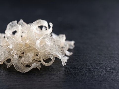 Dried fish maw curls arranged on dark slate surface