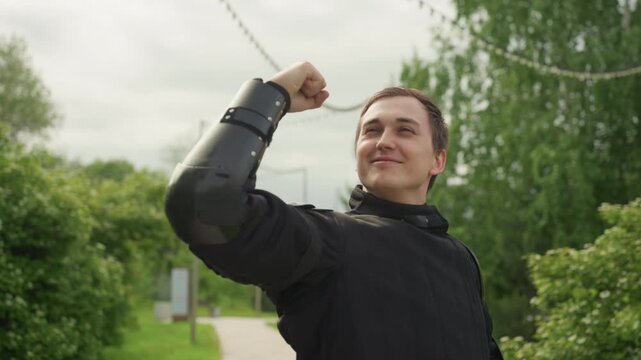 Close up of man wearing black protective arm guards raising his arms and flexing muscles in outdoor park setting with green trees and cloudy sky. subject maintains confident posture