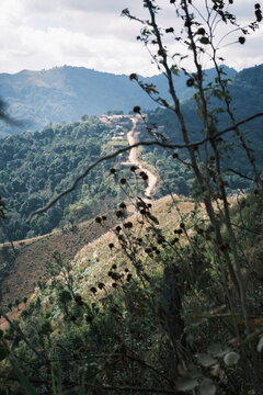 Laos - 30 December 2024: View of a remote Hmong tribe village situated on a mountain ridge, surrounded by lush green hills and a winding dirt path under a cloudy sky.
