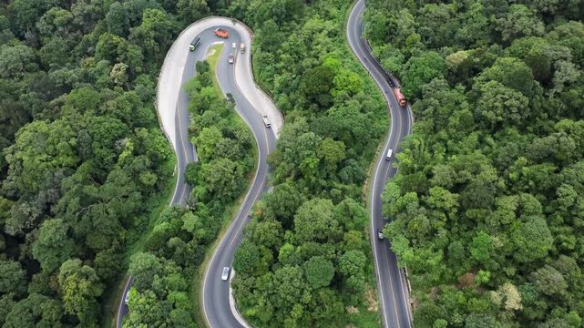 Aerial view of a winding road through the dense forest of Panatapan Berastagi with vehicles traveling along the curves in Berastagi, North Sumatra, Indonesia.