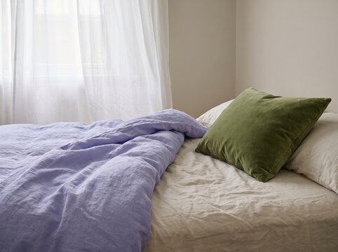 Soft linen bedding with green cushion by sheer curtain