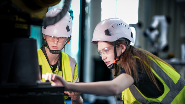 Two female robotics engineers in an R and D lab troubleshoot an artificial intelligence cobot. They are inspecting the robotic system hardware and programming.