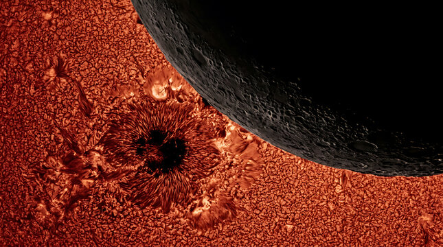 Extreme close-up of sun surface with moon eclipsing large sunspot.