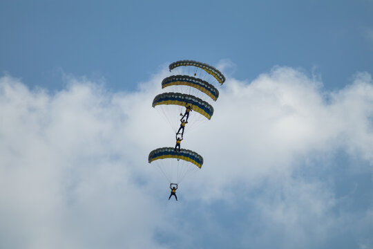 Parachutists formation on airshow with yellow-blue ukrainian parachutes in blue sky with clouds
