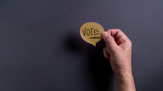 Hand holding a sign that says vote against a dark background during election season in the United States