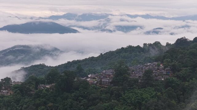 Aerial view of a mountain village nestled in lush green forests surrounded by rolling hills and low-hanging clouds in Puer, Yunnan, China.