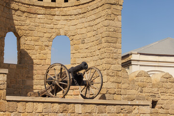 Fototapeta premium Historic cannon rests against ancient stone walls under bright blue sky in a peaceful courtyard