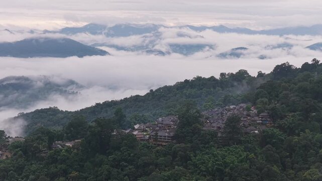 Aerial view of a traditional village nestled among lush green mountains and rolling clouds in Puer, Yunnan, China.