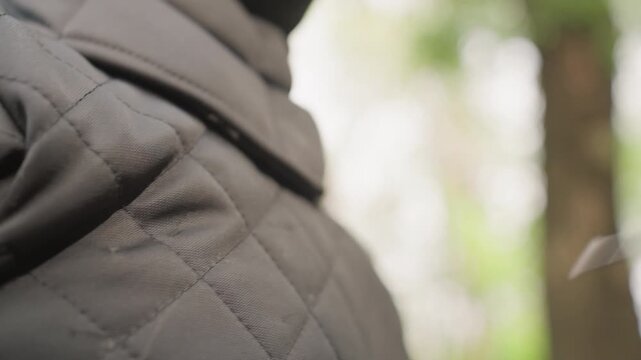 Close up of person wearing dark gray quilted fabric with visible stitching as ice pick is inserted into material. background shows blurred green foliage indicating outdoor setting