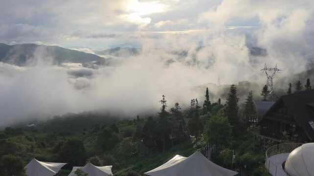 Aerial view of a mountain resort featuring white tents and a dome structure nestled among lush green hills and rolling clouds in Puer, Yunnan, China.
