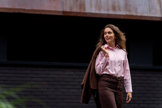 Happy woman holding jacket on shoulder walking in the city