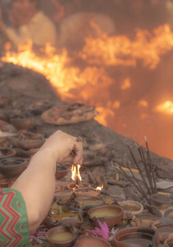 Lahore, Pakistan - 30 March 2019: View of a hand lighting incense sticks amidst numerous burning clay oil lamps at the shrine of Madhu Lal Hussain, creating a warm and glowing atmosphere.