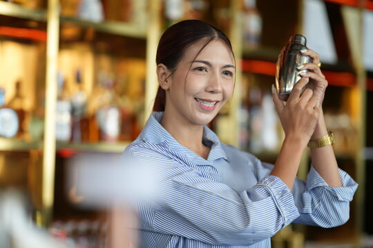 A female bartender at the cocktail bar, mixing a fresh cocktail behind the bar behind a well stocked hotel cocktail bar, in a refined luxury hotel interior, with a warm welcoming look.