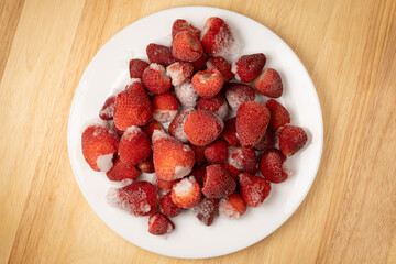 Frozen strawberries on a white plate on a wooden table © Nataliia