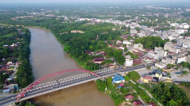 Aerial view of the Wampu River Bridge Binjai - Langsa Toll Road spanning the river with surrounding lush greenery and urban structures in Stabat, North Sumatra, Indonesia.