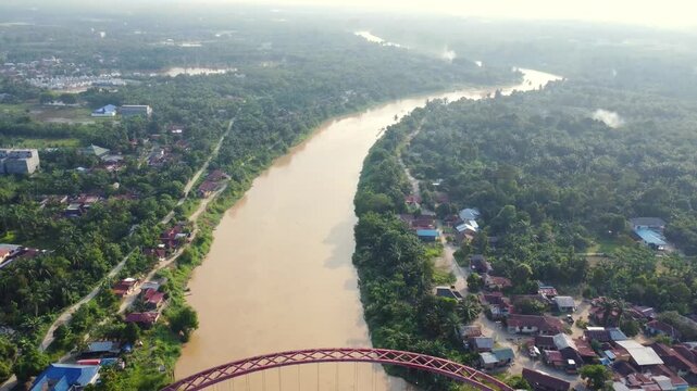Aerial view of the Wampu River Bridge Binjai - Langsa Toll Road spanning the river with lush tropical vegetation and residential areas in Stabat, North Sumatra, Indonesia.