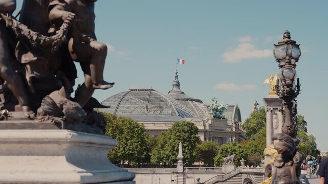 Cinematic view of Grand Palais glass dome with French flag, framed by ornate bronze statues and street lamps of Pont Alexandre III in Paris, France. High quality 4K B-roll video.