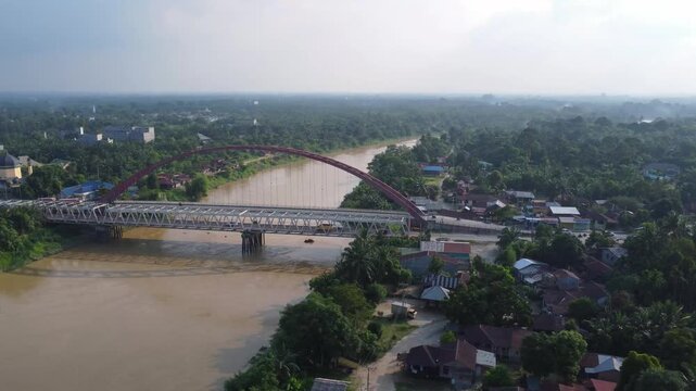 Aerial view of the Wampu River Bridge Binjai - Langsa Toll Road crossing the river with lush vegetation and nearby residential areas in Stabat, North Sumatra, Indonesia.