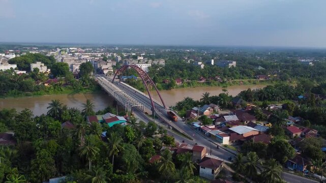 Aerial view of the Wampu River Bridge on the Binjai - Langsa Toll Road spanning the river with lush greenery and residential areas in Stabat, North Sumatra, Indonesia.