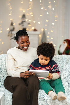 Mother and son relaxing on sofa using digital tablet during Christmas