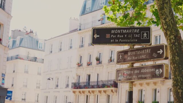 Close up view of brown pedestrian directional road signs guiding towards Montmartre, Rue Lepic, and Theatre des Abbesses with classic Parisian buildings in the blurred background, Paris. 