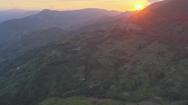 Aerial view of the Yuanyang Rice Terraces during golden hour with lush green hills and mountain slopes in Honghe Hani and Yi Autonomous Prefecture, Yunnan, China.