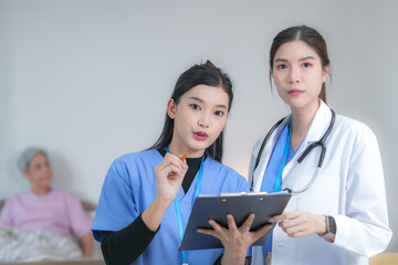 Obraz premium A female nurse in blue scrubs and a female doctor in a white coat review electronic patient records side by side on a touchscreen tablet. A nursing home lifestyle picture.