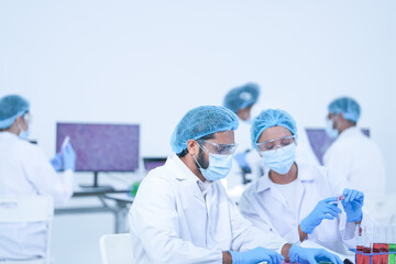 Laboratory coworkers compare liquid samples in a test-tube rack at a clean white laboratory bench...