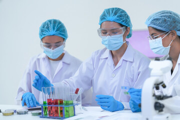 A research duo record microscope findings on a tablet at a laboratory workstation while wearing...