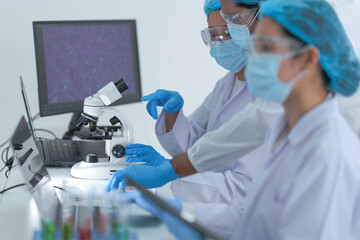 A team of scientists examine a specimen under a microscope at a laboratory workstation while...