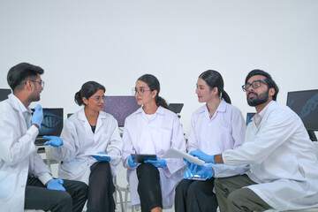 A research team discuss research results as a group in a clean research facility while wearing...