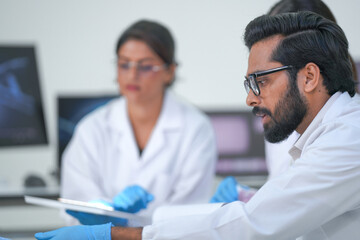 A research team analyse genetic data on a digital tablet before screens displaying a DNA helix...