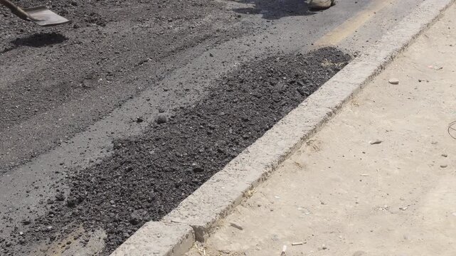 Road construction workers laying fresh hot asphalt on the street using shovels during infrastructure repair and maintenance.